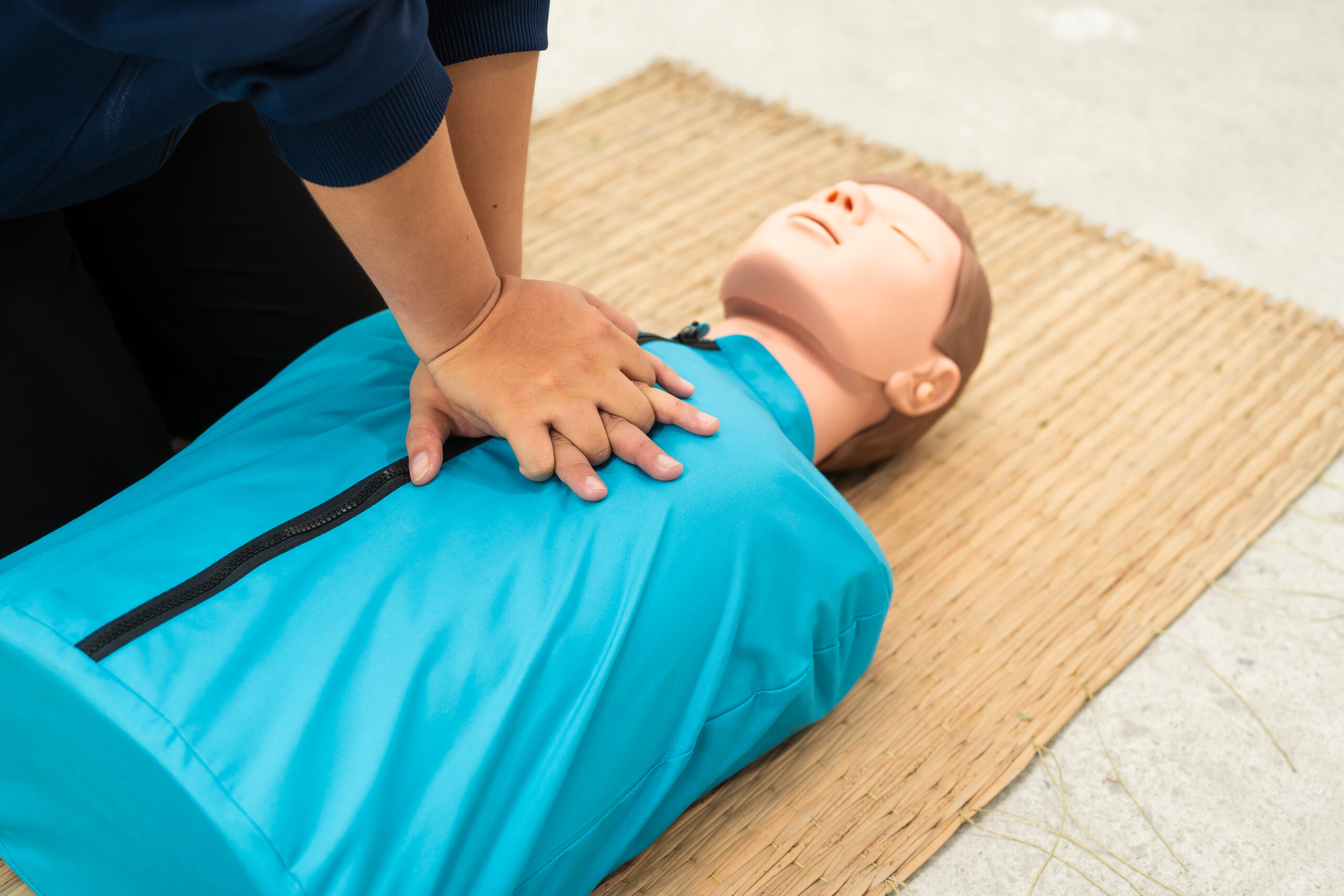 A person practises CPR by pressing their hands on the chest of a training manikin lying on a mat.